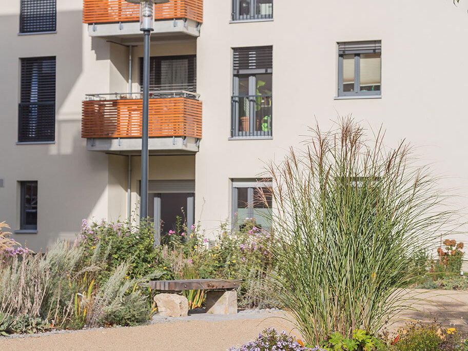 Wohnhausfassade in Jena mit orangefarbenen Balkonen, dunklen Fensterelementen und bepflanztem Außenbereich